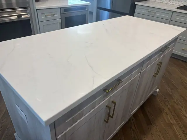 White quartz kitchen island with light gray veining over white cabinets with gold pulls