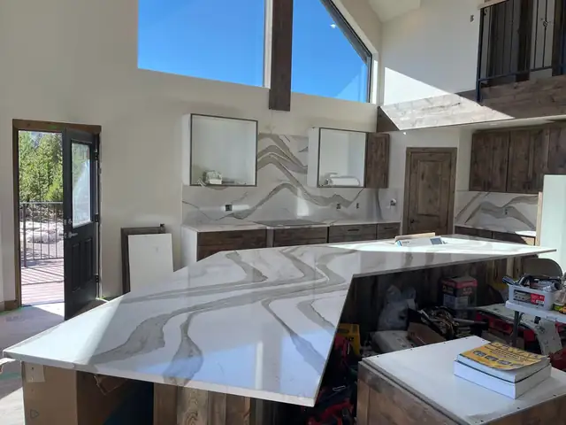 Bold veined white quartz island with full-height matching backsplash in a bright kitchen with tall windows